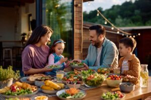 Famille avec enfants en terrasse partageant un repas d'été avec des légumes et des crudités